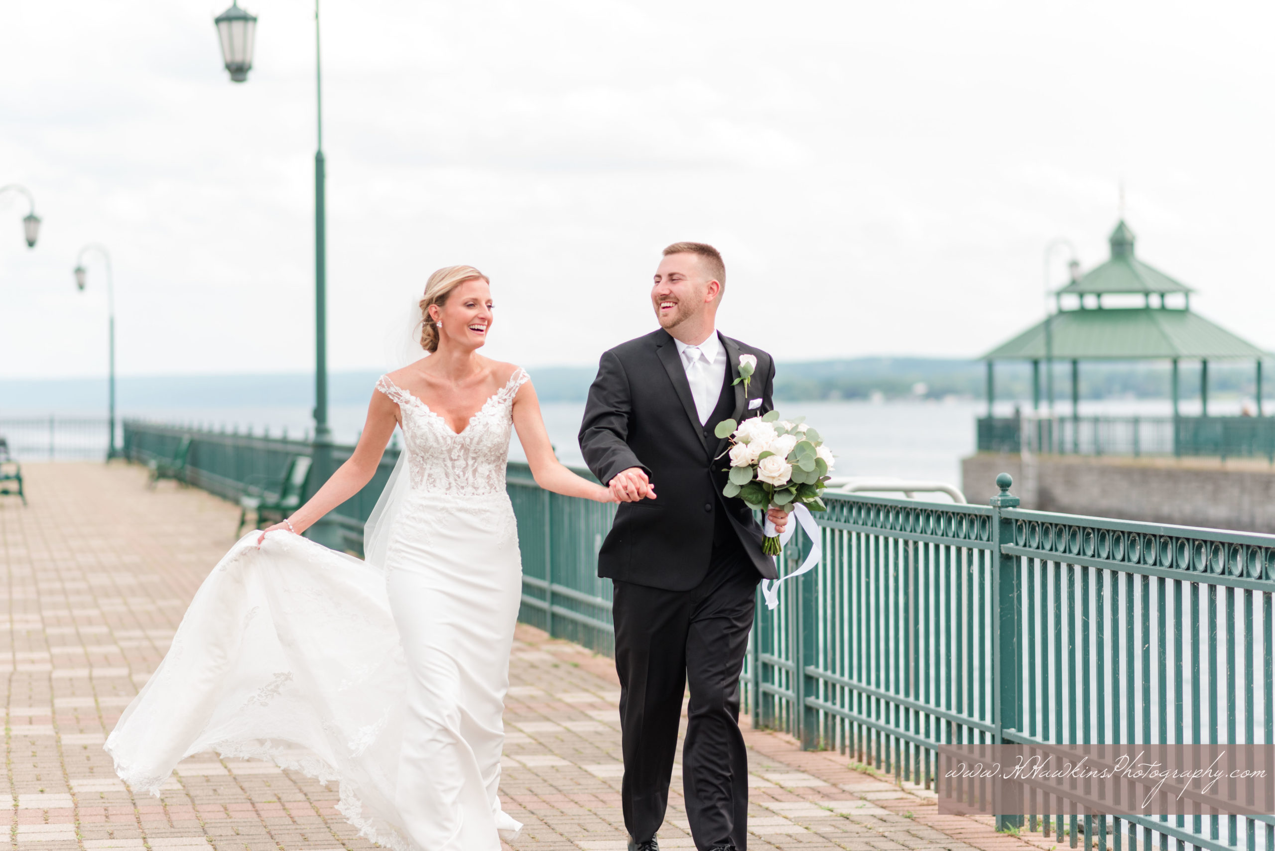 Bride and groom run together on the pier on Owasco Lake at Emerson park pavilion on their wedding day