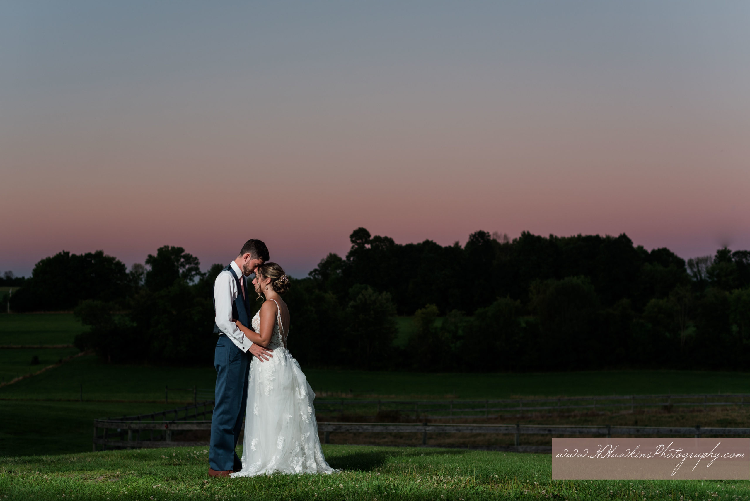 Bride and groom stand in field at Florida barn wedding with pink and purple sunset behind them