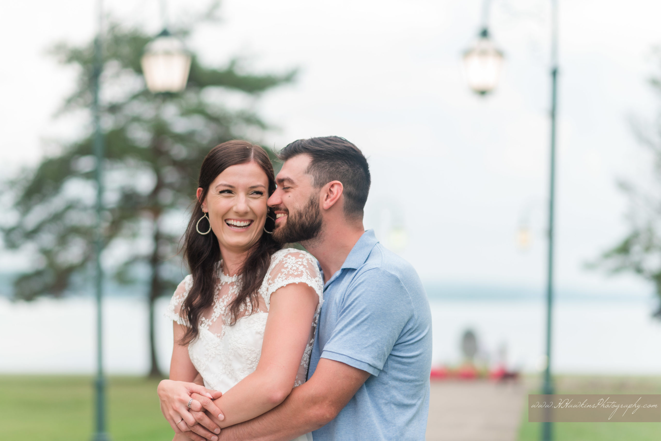 Bride and groom to be stand together on sidewalk with lake in background by Orlando engagement photographer