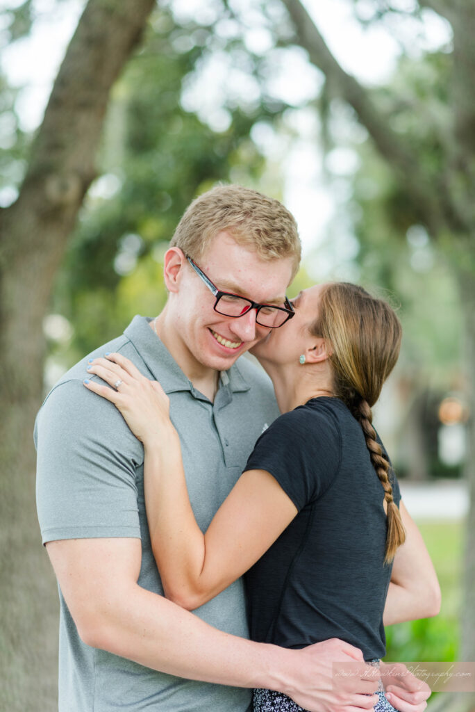 Bride makes groom laugh along a tree lined walk way for their Celebration FL engagement photos
