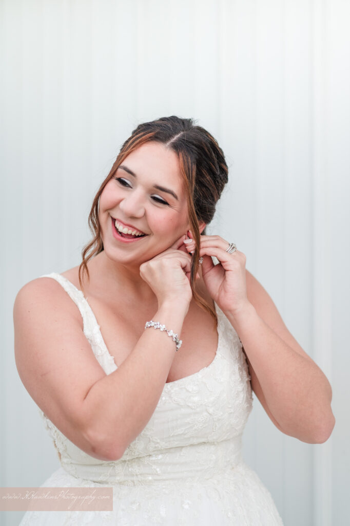 Bride puts on her earrings as she laughs outside of bridal suite at Acres of Grace Family Farms wedding venue