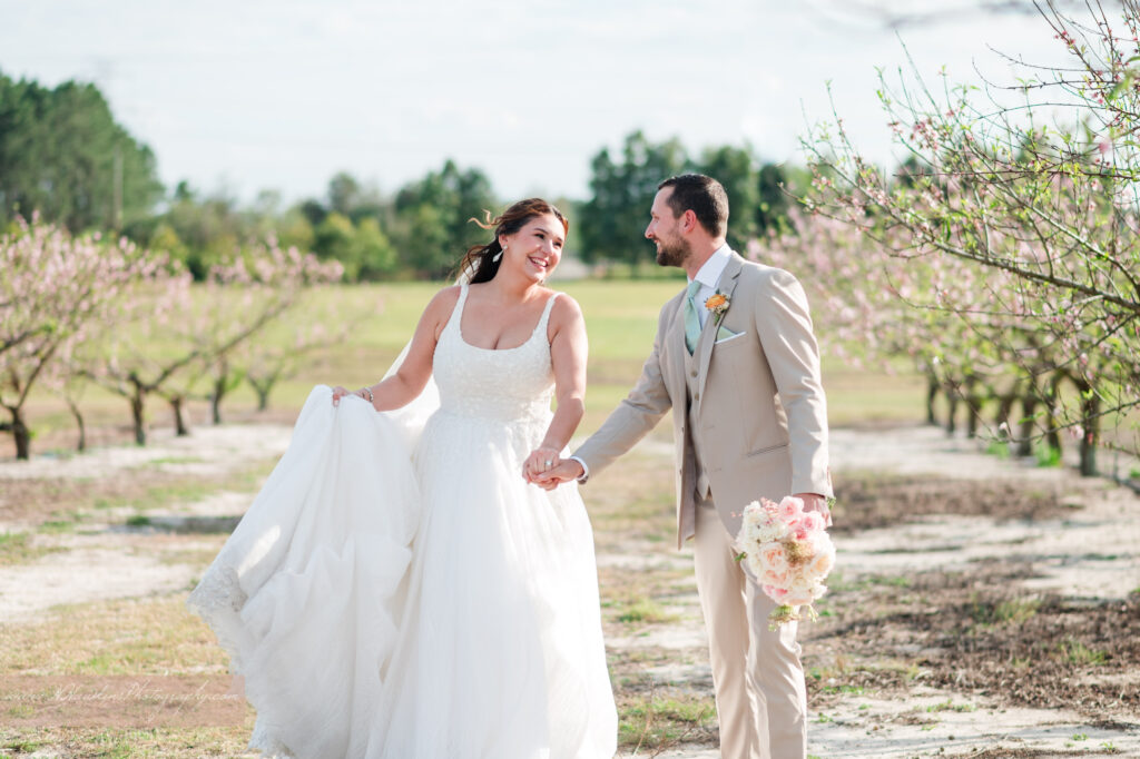 Bride and groom run through peach blossom orchard at Acres of Grace Family Farms in Howey in the Hills FL