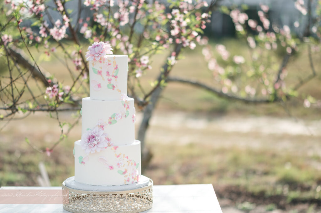 Gorgeous wedding cake with gold flecks, pink blossoms on it by Bells Cake House at Acres of Grace wedding venue in Howey in the Hills FL