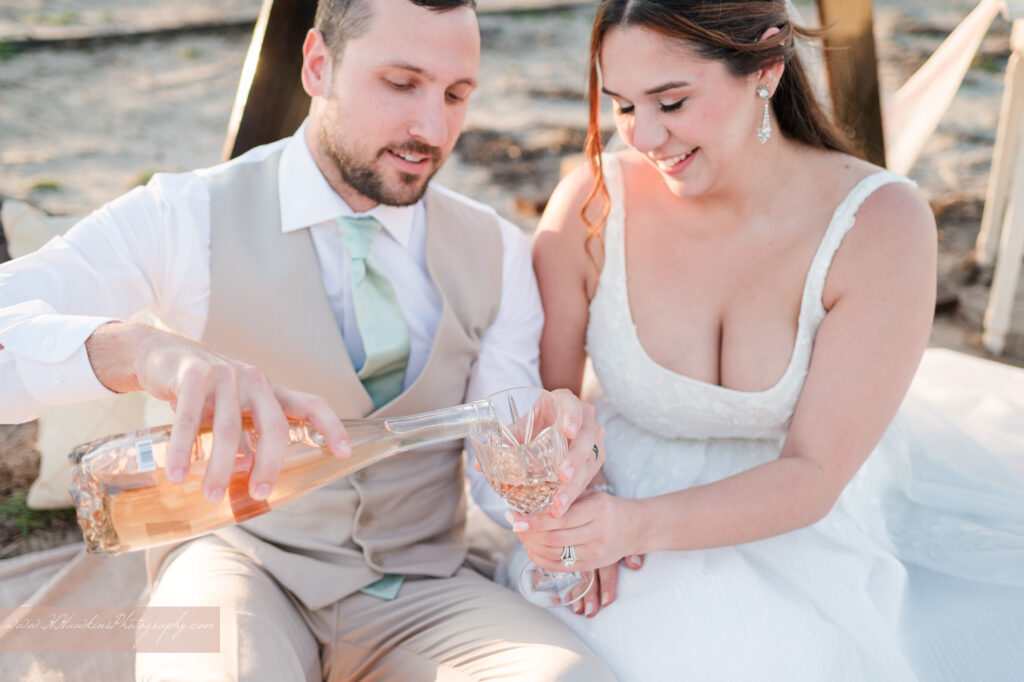 Bride and groom pour champagne at their wedding reception to enjoy with their wedding cake at peach blossom orchard at Acres of Grace wedding venue