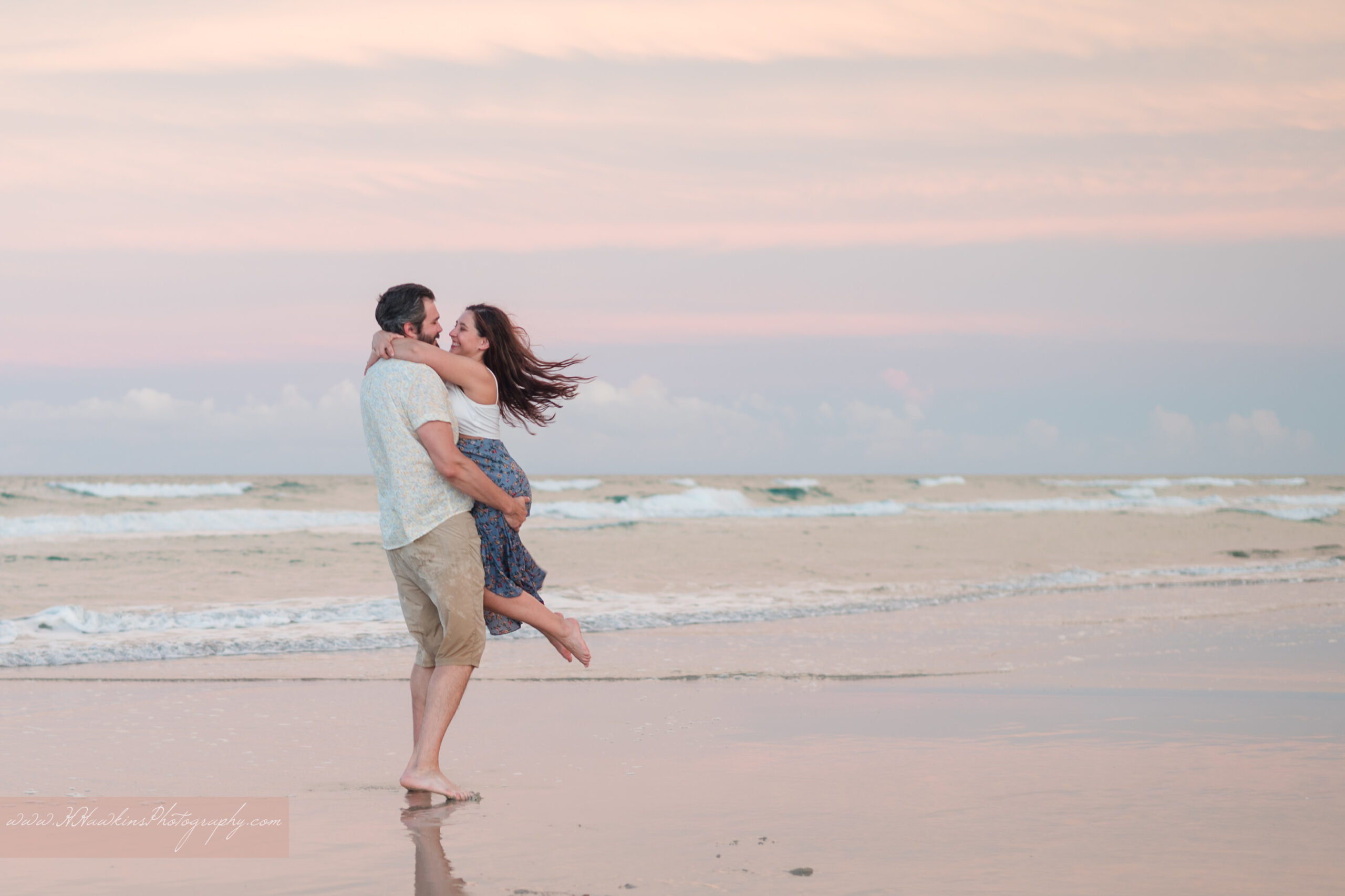 Groom lifts bride up and spins her, with hair flying out beside the ocean at Grayce K Barck North Beach Community Park by New Smyrna Beach Photographer