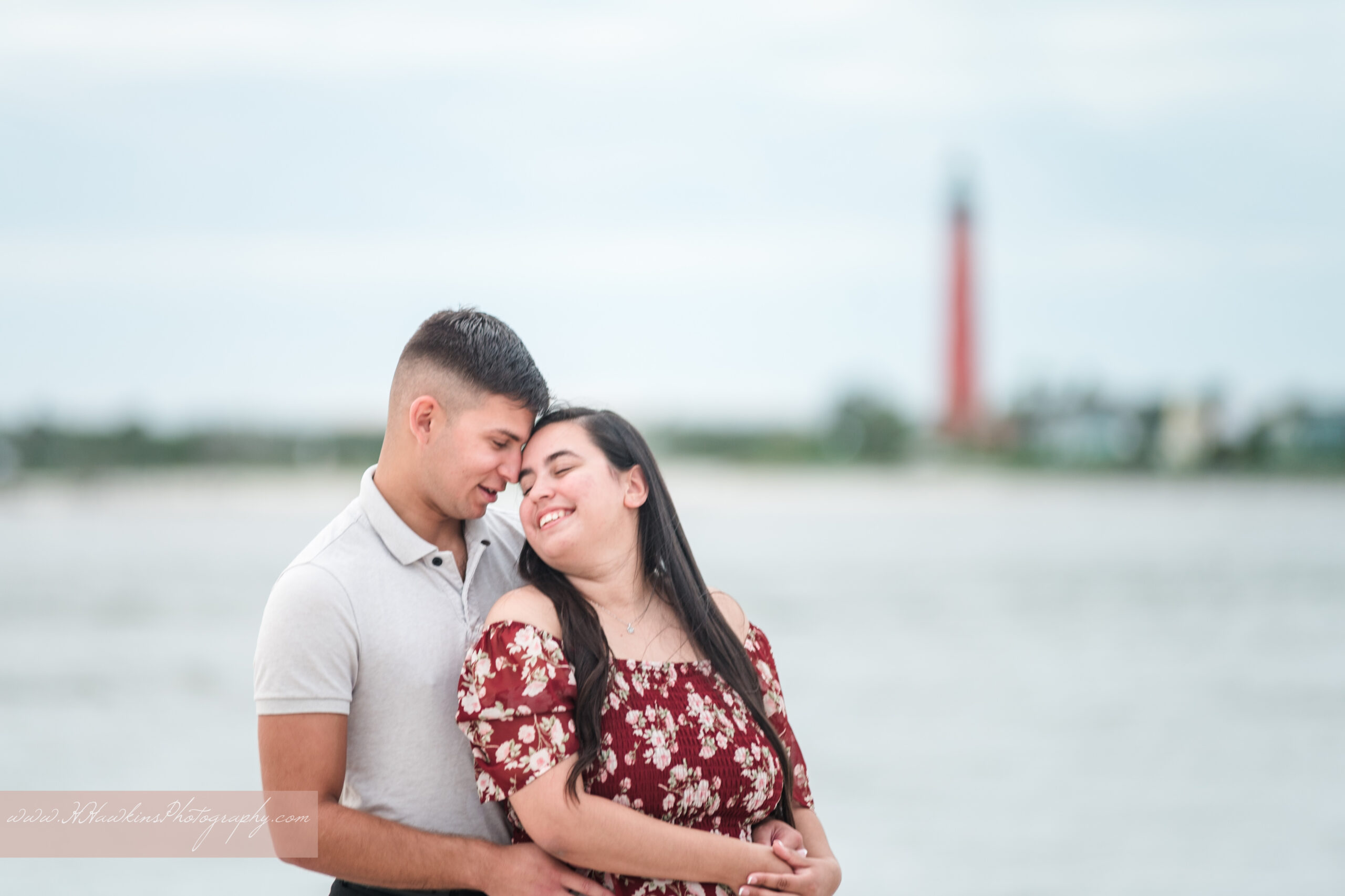 Engaged couple on beach with Ponce Inlet lighthouse in backgroundby Volusia County photographer