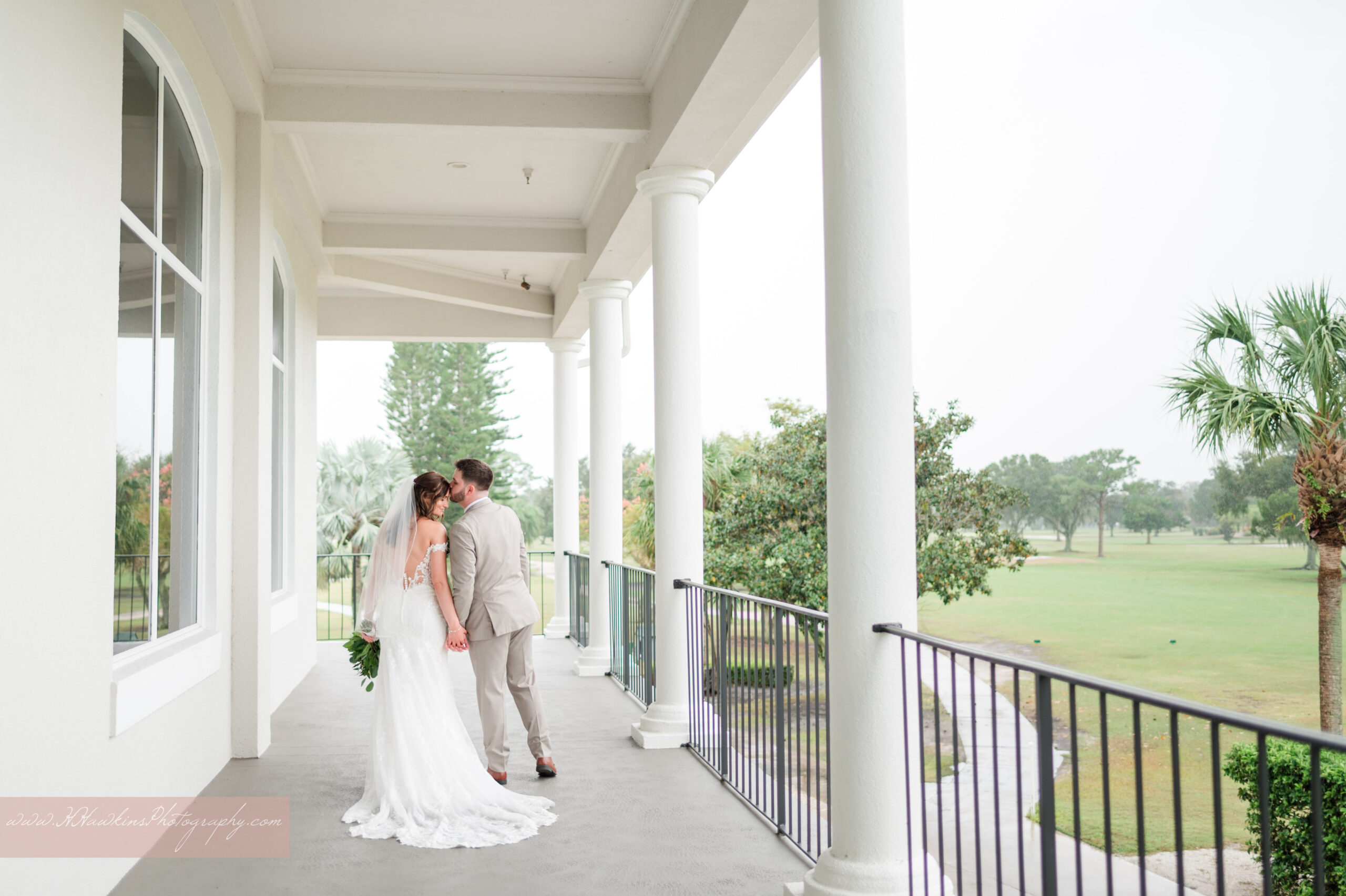 Gorgeous portraits of bride in white wedding dress with light pink bouquet and groom under covered second floor balcony of Rockledge Country Club