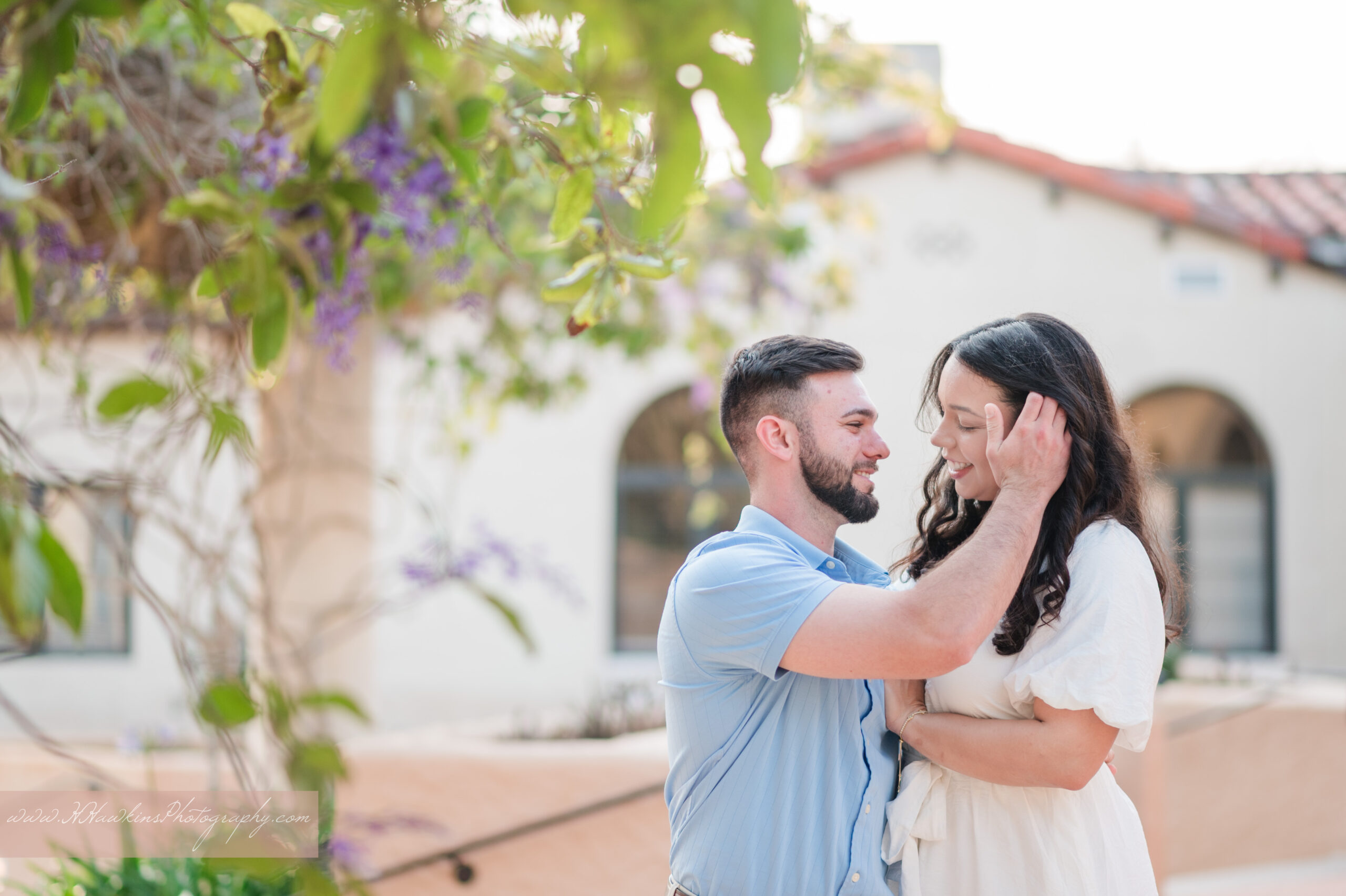 Bride and groom to be kiss in front of purple wisteria at Rollins College near the Rice Family Pavilion