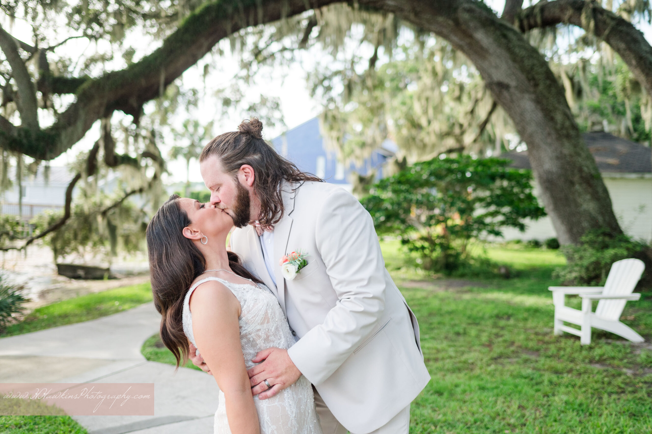 Bride and groom dip kiss under live oak trees whose branches arch over the sidewalk and spanish moss hangs down at the Lakeside Inn in Mount Dora FL by Orlando wedding photographer