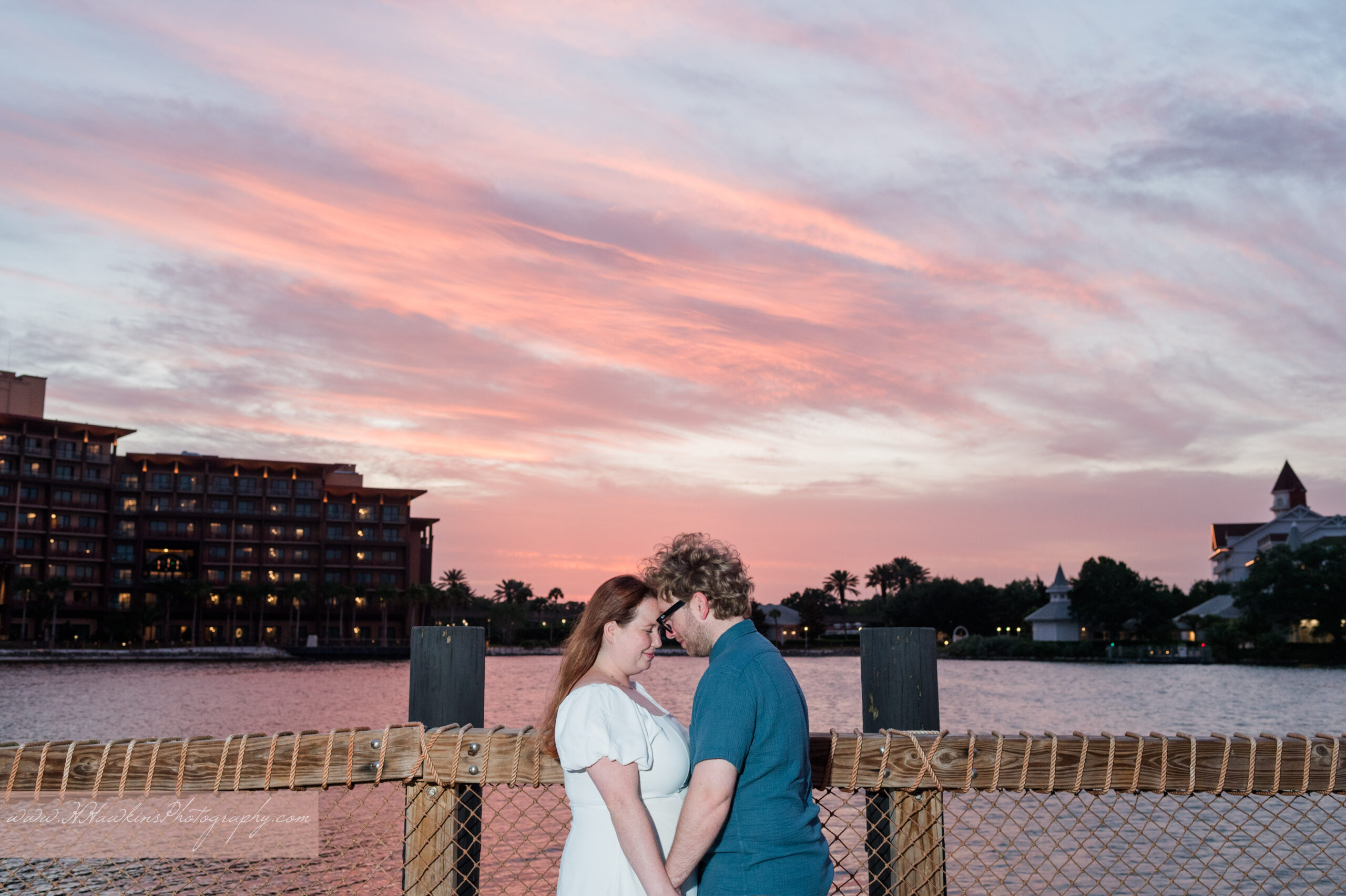 Bride and groom smile at each other as the sun sets over Bay Lake with the Wedding Pavilion and the Grand Floridian in the background